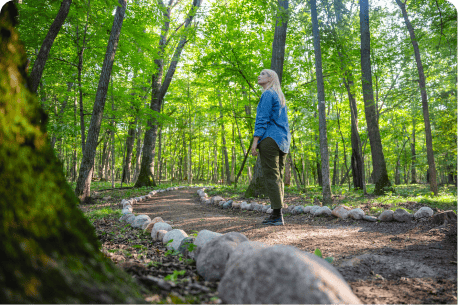 Woman walking along a forest path after a nature memorial, looking up into the trees and reflecting in the peaceful surroundings.